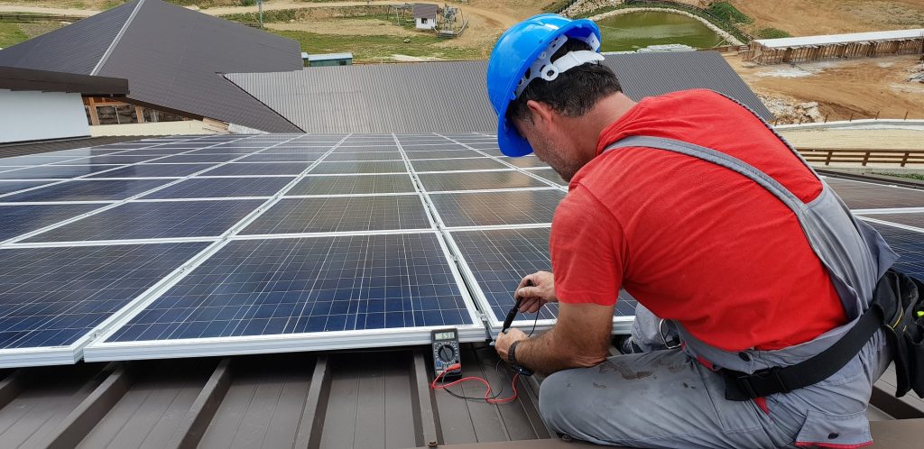 En arbetare installerar solpaneler på taket av ett hus.